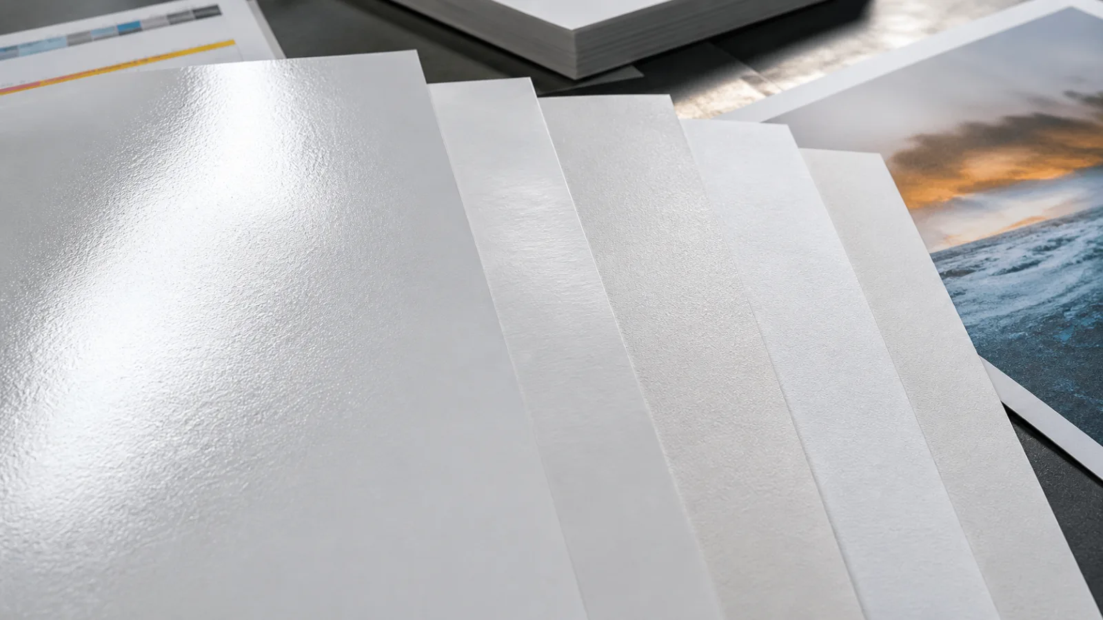Overlapping coated paper sheets showing gloss, silk and matte reflections under directional light